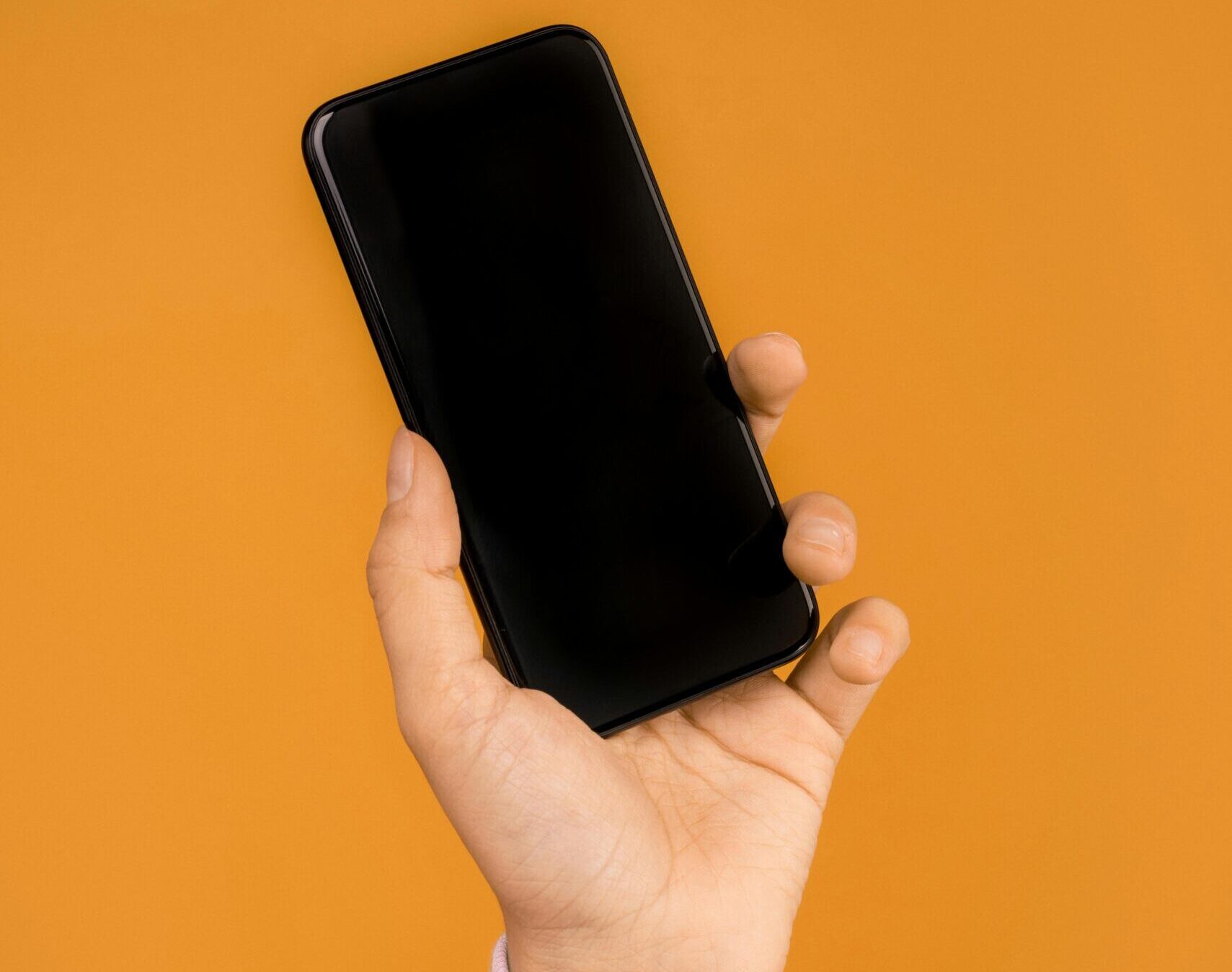 Close-up of a hand holding a smartphone against a bright orange backdrop, emphasizing modern technology.