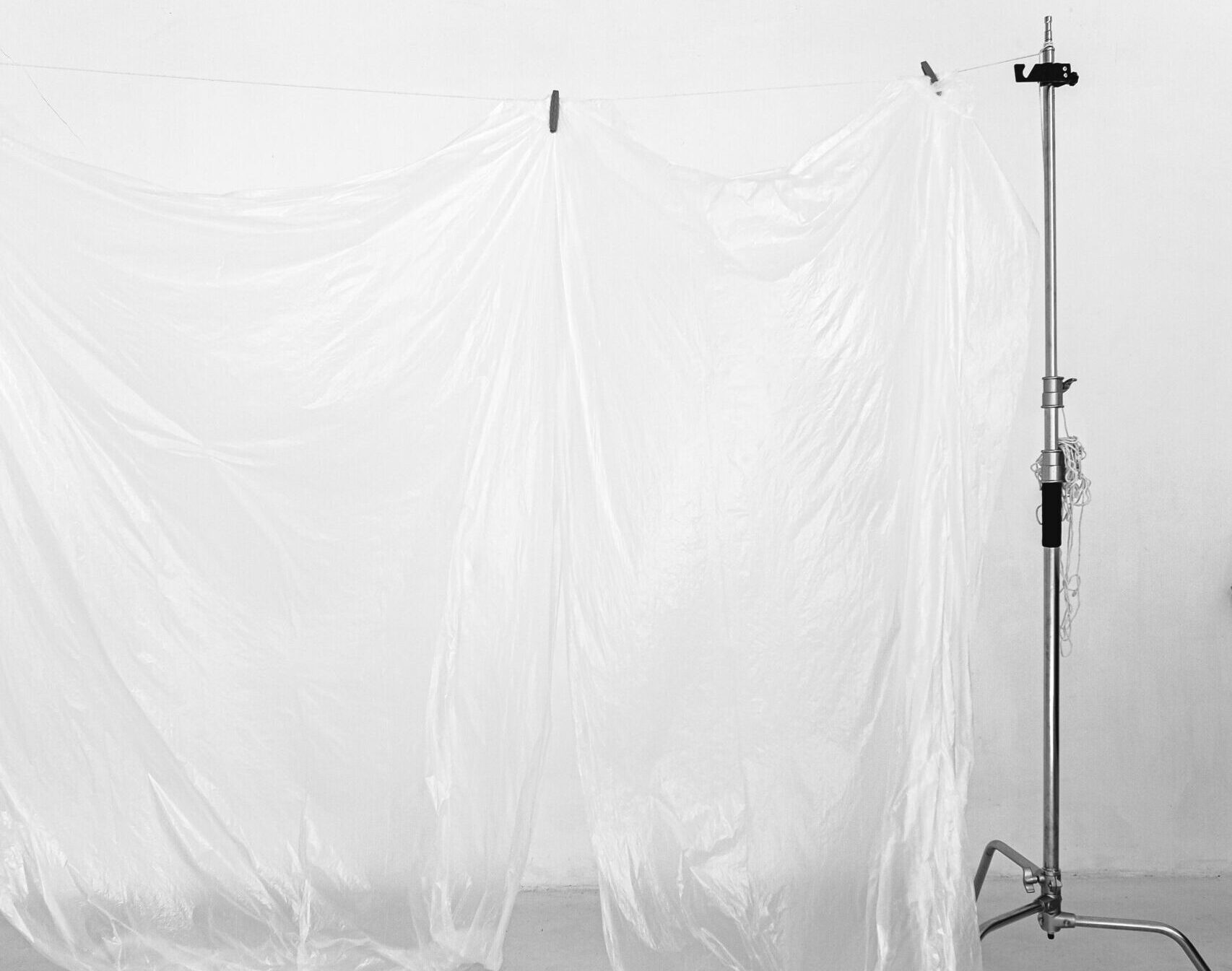 Elegant minimalist composition of a white fabric sheet hanging on a metal stand in an indoor studio setting.